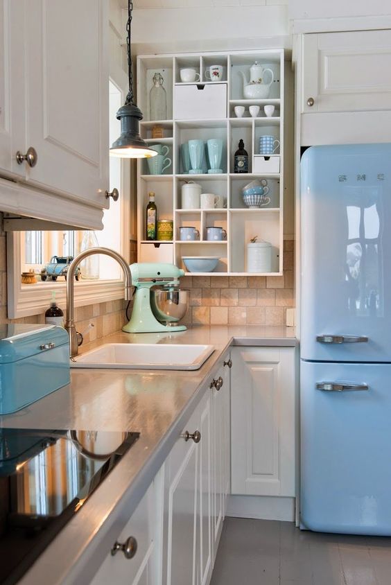 a retro kitchen with white shaker style cabinets, grey countertops, an open storage shelf, a blue fridge and blue and mint touches here and there