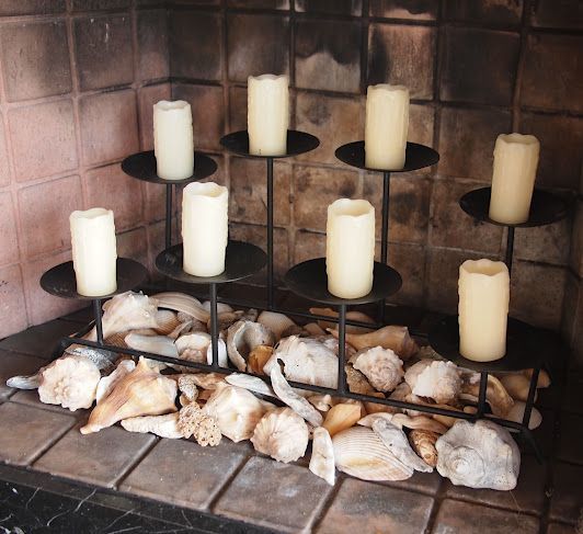 a seaside style fireplace filled with seashells and with a modern candelabra with pillar candles