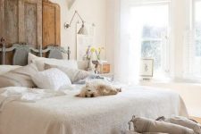 a shabby chic farmhouse bedroom with a vintage door headboard, a basket for storage and much natural light
