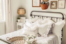 a small and cozy Provence bedroom with a metal bed with grey and white bedding, a chic vintage gallery wall, a small nightstand with a table lamp