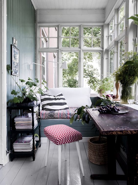 a small and cute vintage sunroom with a built-in bench, dark furniture, potted greenery and a basket