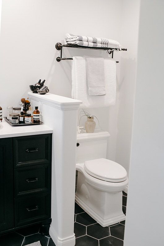 a small farmhouse bathroom clad with black hex tiles on the floor, with a half wall to separate the toilet and a black vanity
