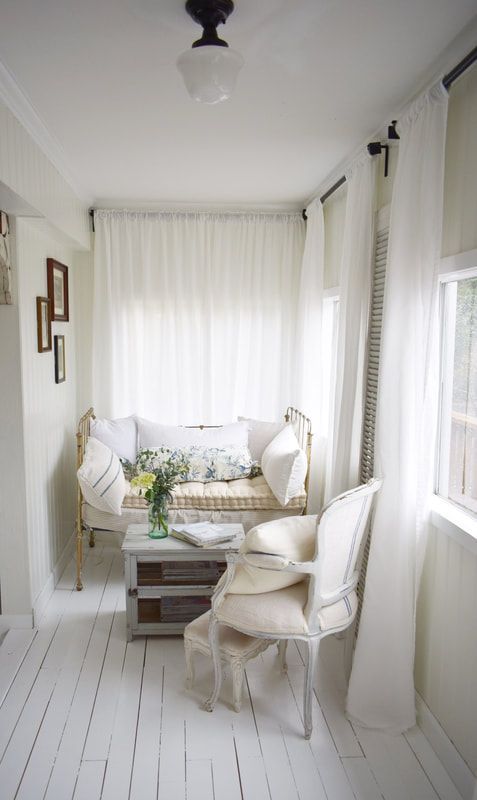 a small white vintage sunroom with a forged daybed and a wooden chair, neutral textiles and a gallery wall