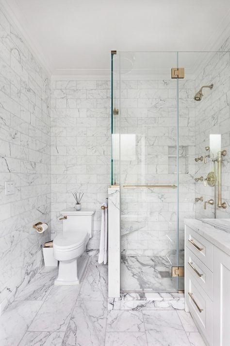 a sophisticated wihte marble tile bathroom with a shower space with a half wall, a white vanity and gold touches for more elegance