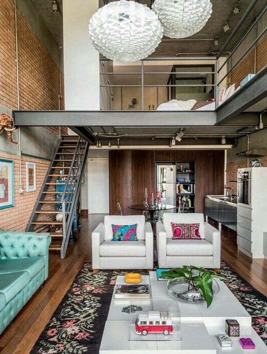 A stylish mid century modern home with a brick accent wall, white furniture and a turquoise sofa, a bright rug and pillow, a sleeping and shower zone upstairs
