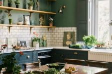 a stylish vintage kitchen with green walls, white subway tiles, teal cabinets, a dark stained dining set, a crystal chandelier and potted greenery
