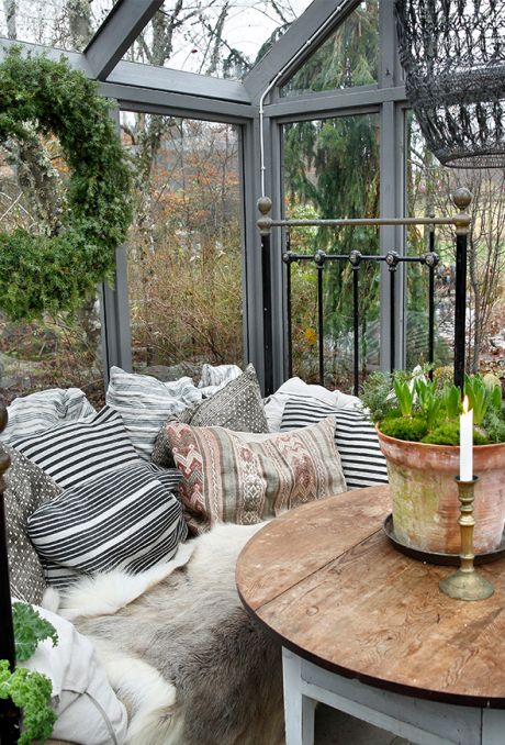 a vintage Scandinavian sunroom with wooden furniture, printed pillows, faux fur, greenery and candles