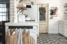 a vintage cottage kitchen in neutrals, with planked cabinets, stained shelves, a mosaic tile floor, metal pendant lamps and pans
