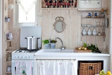 a vintage cottage kitchen with a checked floor, neutral stained walls, open and usual cabinets, baskets and fun textiles