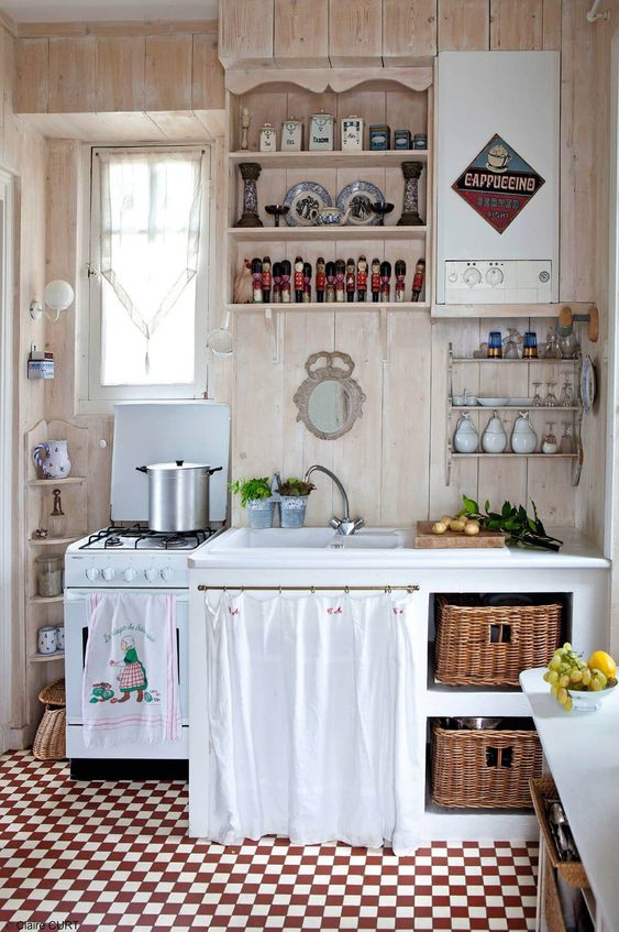 a vintage cottage kitchen with a checked floor, neutral stained walls, open and usual cabinets, baskets and fun textiles