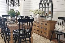 a vintage farmhouse dining space with black chairs, a light stained buffet and table, a metal chandelier