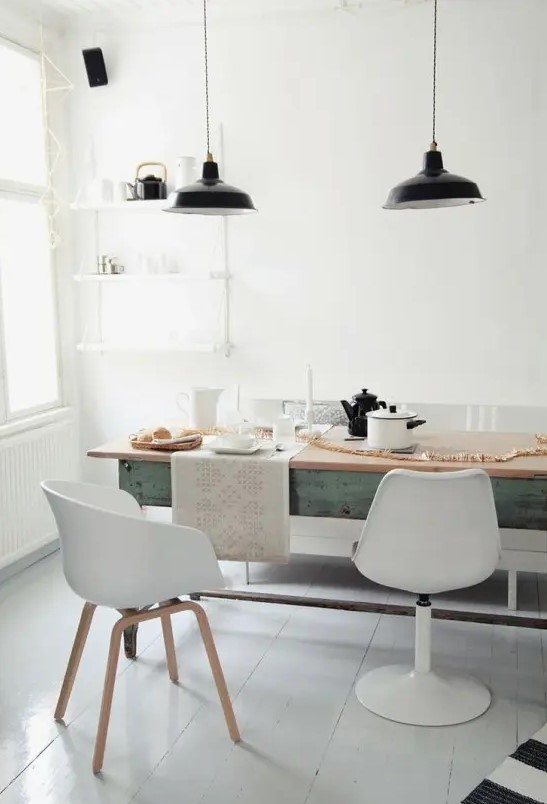 A vintage inspired Nordic dining room with a long blue table, mismatching white chairs, a lightweight wall shelf and black pendant lamps