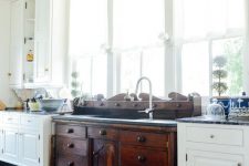 a vintage kitchen with white cabinets, a dark stained vanity of a vintage dresser, pendant lamps, printed rugs and lots of windows