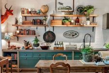 a vintage rustic kitchen with teal and stained cabinets, a stained dining set with vintage chairs, open shelves and an orange faux taxidermy piece