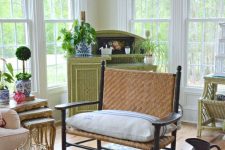 a vintage rustic sunroom with green and neutral wicker furniture, neutral textiles, potted greenery and a floral rug