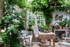 a vintage rustic sunroom with wooden furniture, printed textiles, potted greenery and blooms and lots of greenery