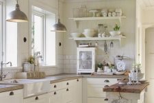 a vintage white Scandinavian kitchen with a small kitchen island, butcherblock coutnertops, a white subway tile backsplash, open shelves and pendant lamps