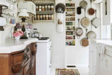 a vintage white kitchen with a stained buffet as cabinetry, white cabinets, white beadboard walls, open shelves and vintage pans for decor