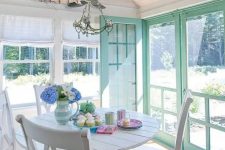 a white farmhouse sunroom with mint window frames, neutral textiles, a vintage chandelier and pastel touches