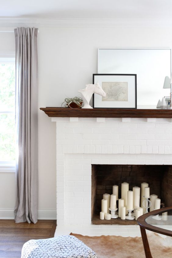 a white fireplace with a dark stained mantel and white pillar candles in the fireplace and on candle holders