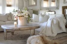 a white shabby chic living room with a gallery wall of mirrors, white furniture, a shabby table and lamps and blooms