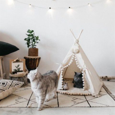 a white teepee with pompoms is a creative and fun cat bed and house in one, perfect for a boho interior