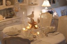 a white vintage dining room with elegant furniture, a crystal chandelier, some porcelain and glass and a cool lamp