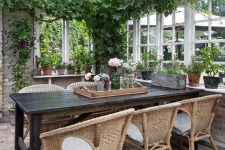 an enchanting vintage sunroom with a black table, wicker chairs, potted greenery and blooms and suspended lamps