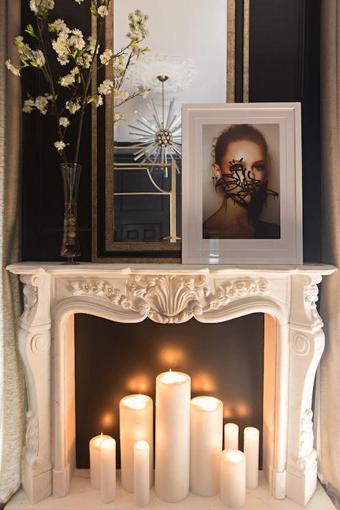 an ornate carved marble fireplace mantel filled with lit candles in front of a black backdrop that highlights them