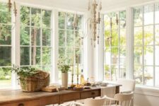 a French country dining room with a gallery of windows, a large stained table and vintage white chairs plus chandeliers