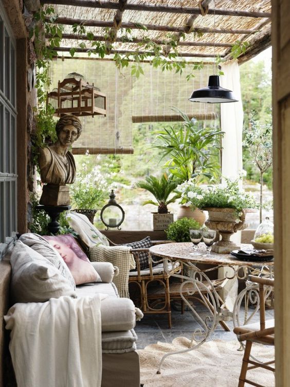 A Provence inspired terrace with rattan and metal furniture, neutral and pastel textiles, potted greenery and blooms and some pendant lamps