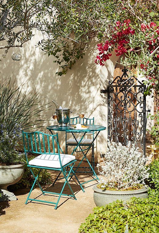 A Provence inspred outdoor space with a green metal table and chairs, potted plants and blooms and some lanterns