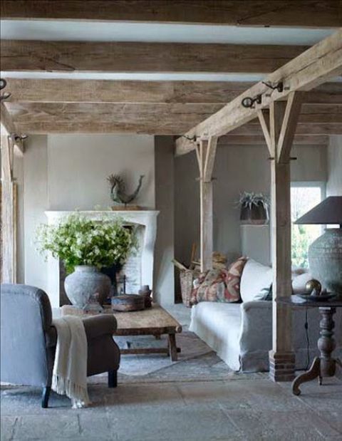 a Provence living room with wooden beams and pillars, with a fireplace and a white sofa plus a blue chair and cool lamps
