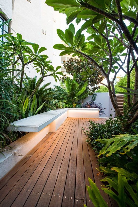 A beautiful minimalist deck with a built in bench, potted greenery, trees and plants, with built in lights is amazing