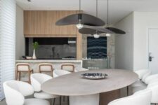 a beautiful minimalist dining room with an oval table and rock legs, creamy curved chairs, black pendant lamps