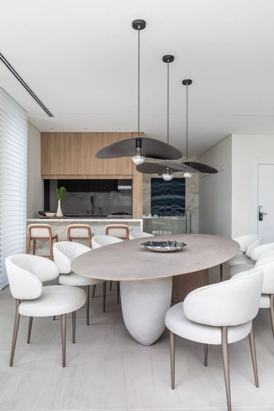 a beautiful minimalist dining room with an oval table and rock legs, creamy curved chairs, black pendant lamps