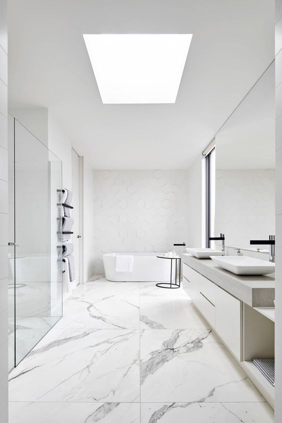 a chic white minimalist bathroom with marble large scale tiles, white furniture, white appliances and white hex tiles