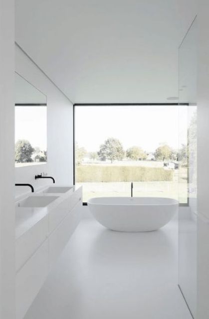 a clean all-white minimalist bathroom with a glazed wall, a white floating vanity, white appliances and black fixtures