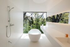 a concrete creamy bathroom with large scale tiles, a long floating vanity and a glazed wall for rainforest views