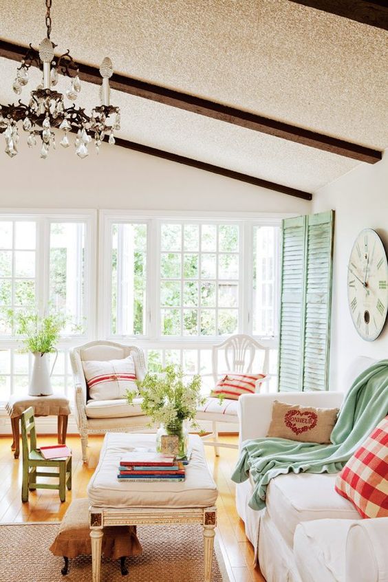 a cottage Provence with green shutters, neutral furniture, plaid and green textiles, a crystal chandelier and a jute rug