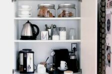 a home tea and coffee bar with all the necessary appliances and various cups and cookies hidden inside a kitchen cabinet