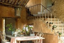 a large farmhouse table and white forged chairs, a large lantern over them, a watering can and some greenery and blooms to highlight that refined French feel