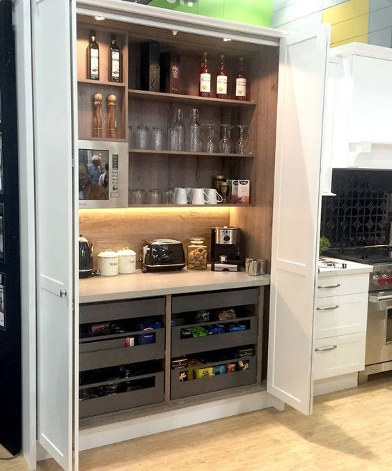 a large storage unit with open shelves and drawers, appliances, mugs, glasses, wine and other stuff is a good space for cooking here