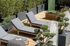 a lovely minimalist terrace with a wooden deck, black loungers, potted plants and blooms and a mini garden shower is cool
