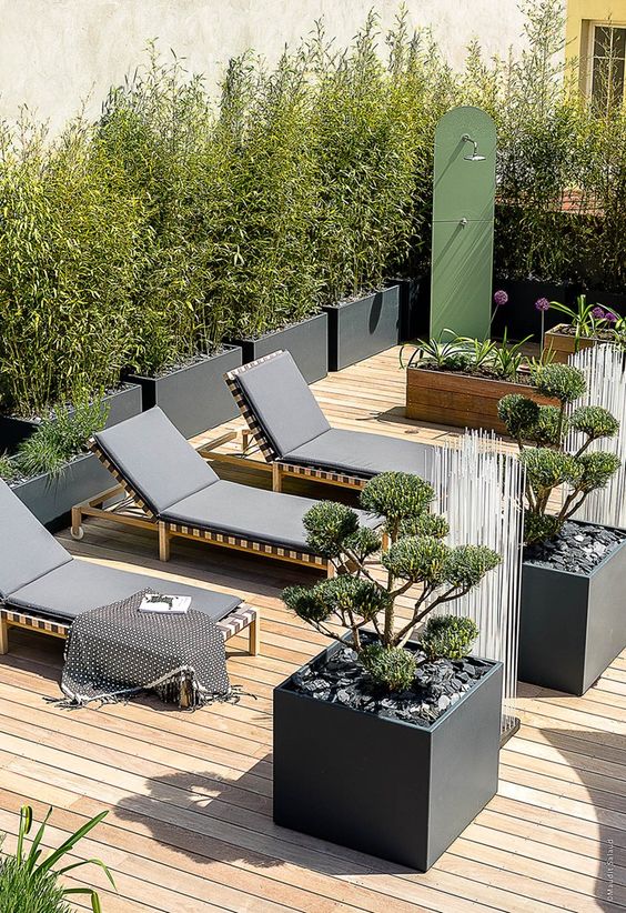 a lovely minimalist terrace with a wooden deck, black loungers, potted plants and blooms and a mini garden shower is cool