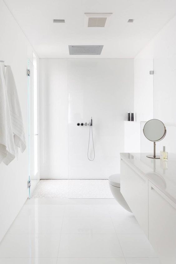 a minimal white bathroom clad with large scale tiles, a floating vanity, a a frosted glass window, some mirrors