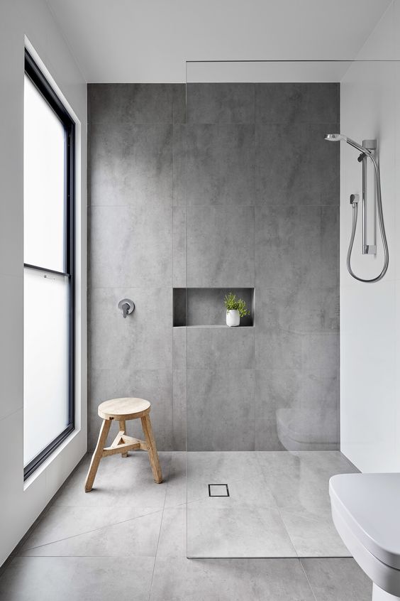 a minimalist bathing space with grey tiles, a frosted glass window, white appliances and a nice for storage