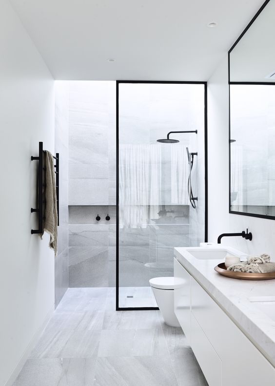 A minimalist bathroom clad with grey stone like tiles, a floating vanity with a stone countertop, a shower with a skylight