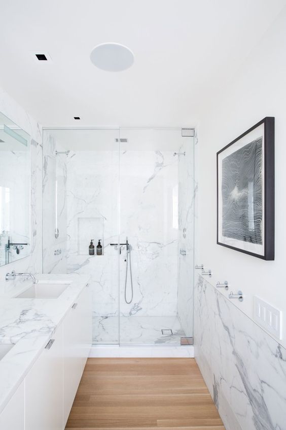 a minimalist bathroom clad with white marble, with a large floating vanity, a statement artwork