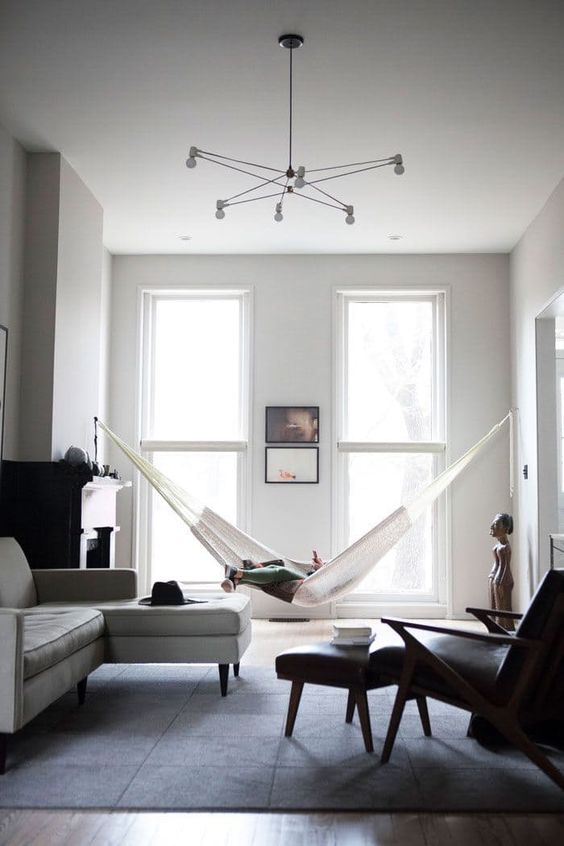 a minimalist black and white living room with neutral and black furniture, a hammock, a fireplace and a catchy chandelier